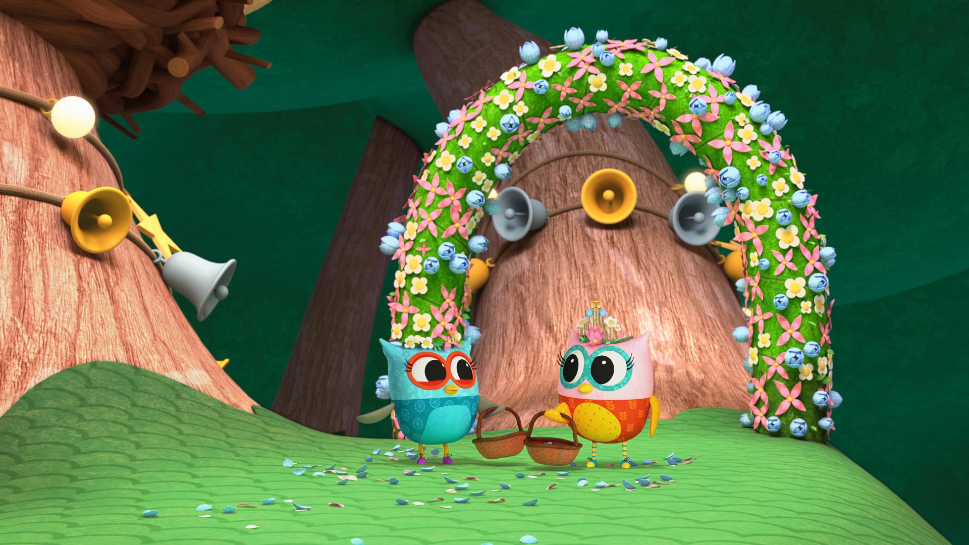 Eva the Owlet and her friend in front of a floral arch and tree decorated with bells