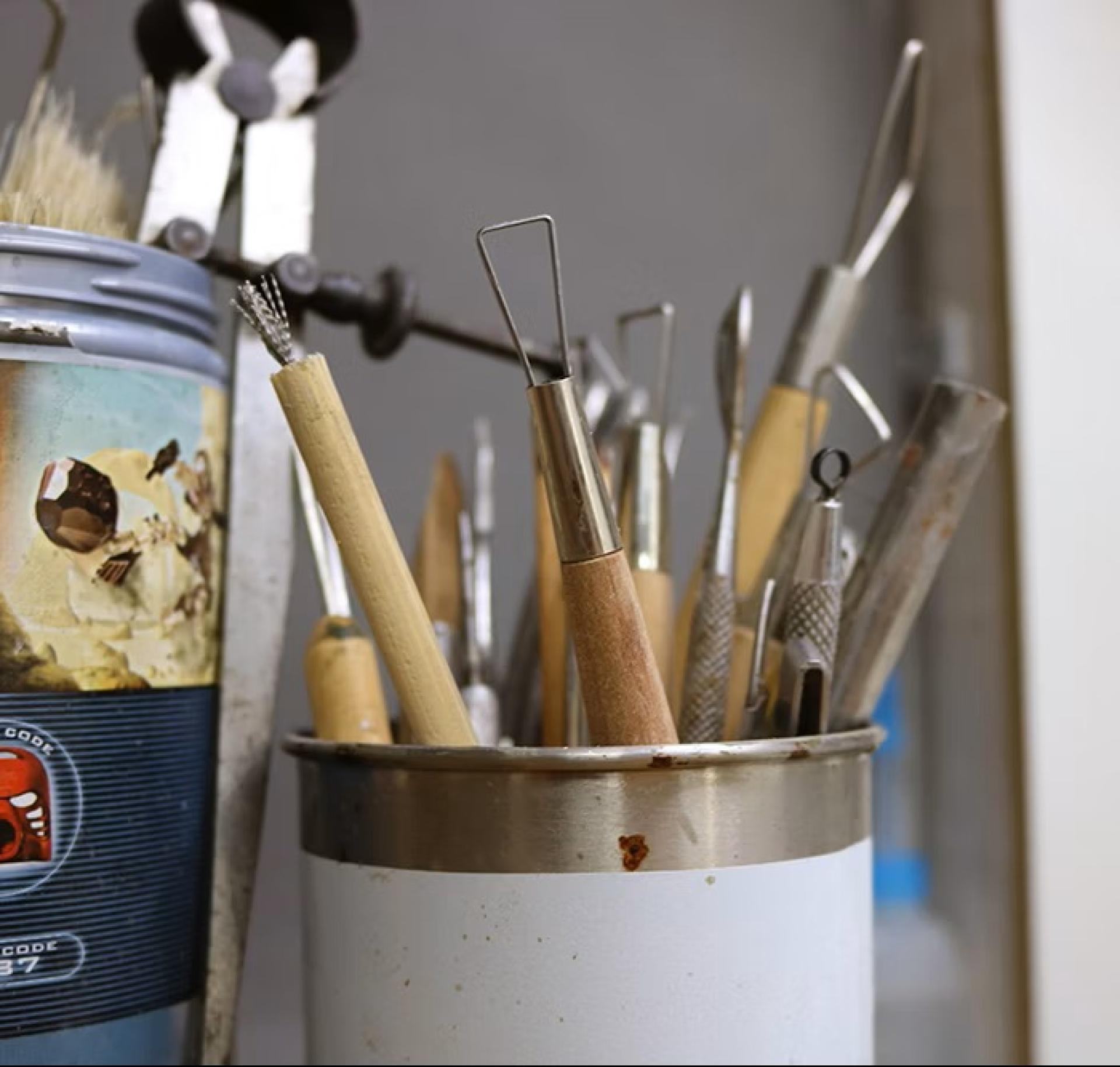 Sculpting tools in a metal container, including wire loop tools and brushes for clay modeling.