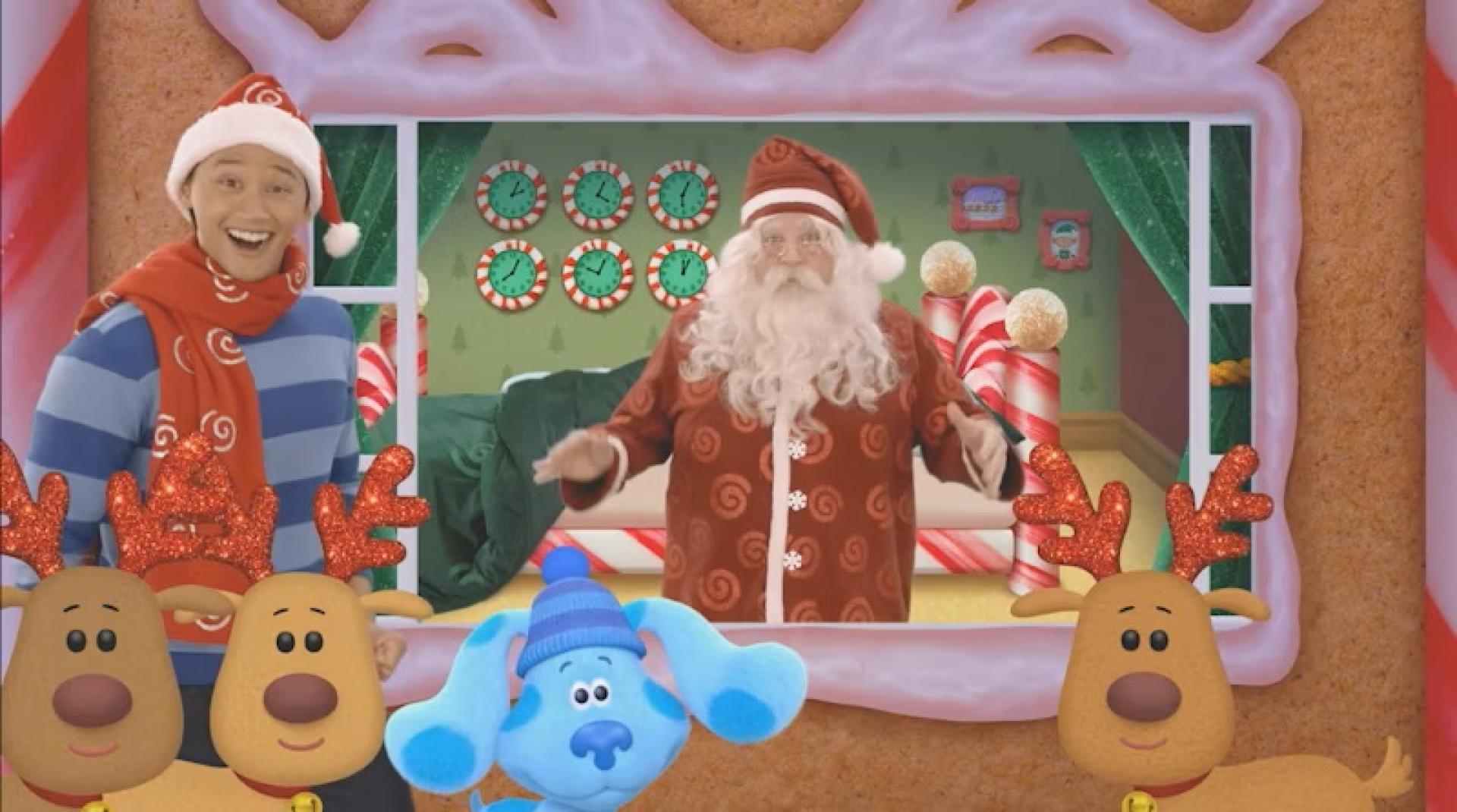 Blue and Josh in front of a gingerbread-style window frame with Santa's reindeers and Santa in the background wearing pajama's in a holiday-themed room.
