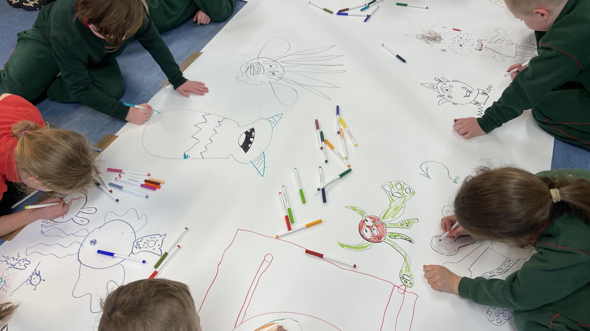 Children coloring large character outlines on a white sheet with scattered markers.