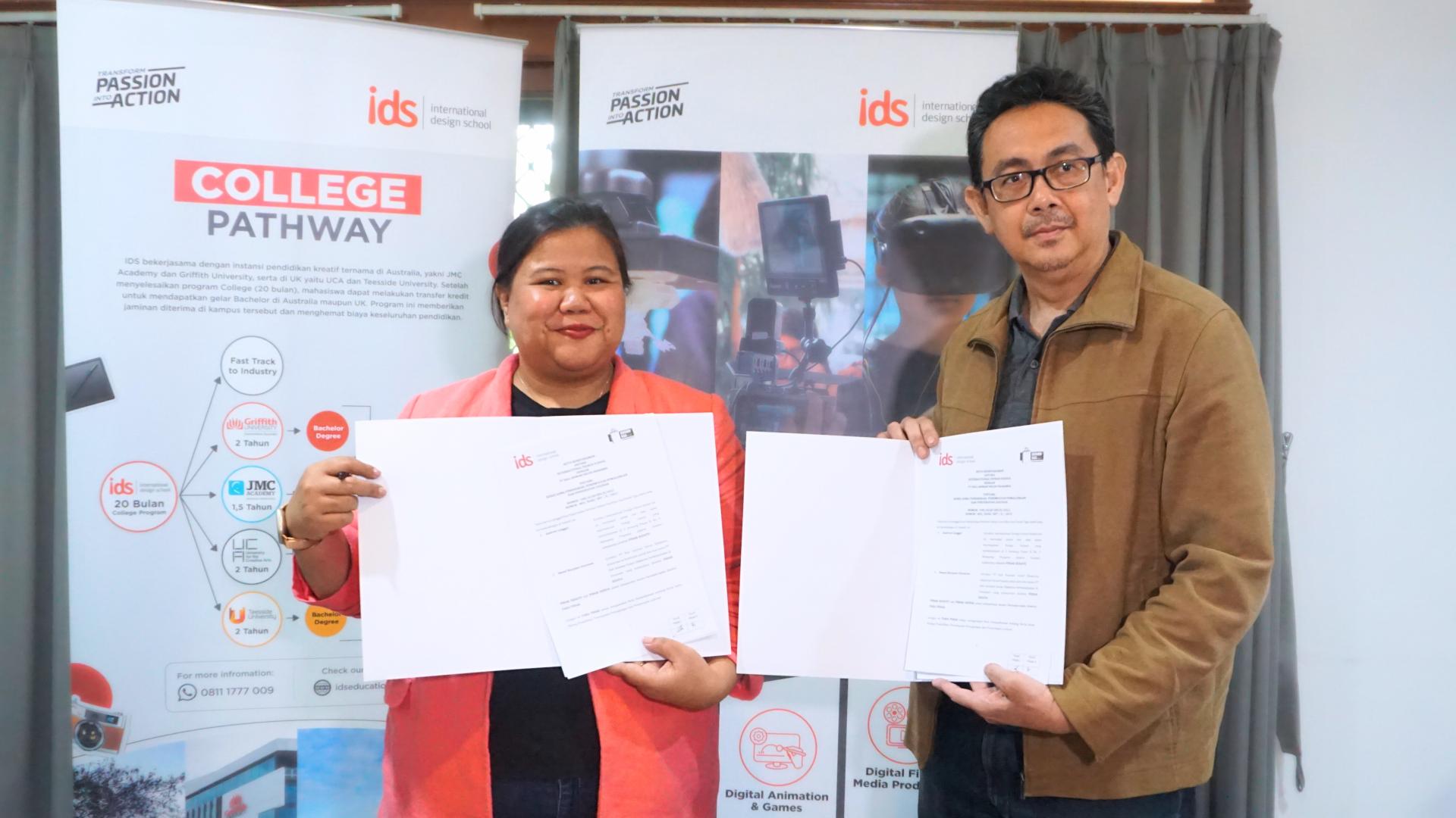 Two people holding signed documents in front of IDS College Pathway banners.
