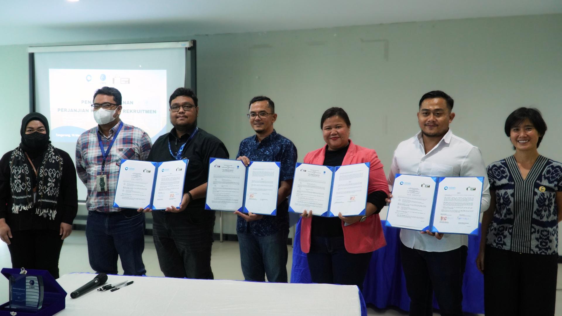 Group of people holding signed documents in front of a presentation screen during a formal agreement session.