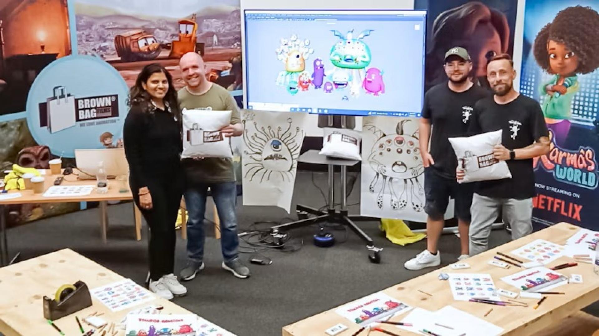 Workshop setting with tables, art supplies, and Brown Bag Films staff members holding pillows featuring Brown Bag Films' logo.