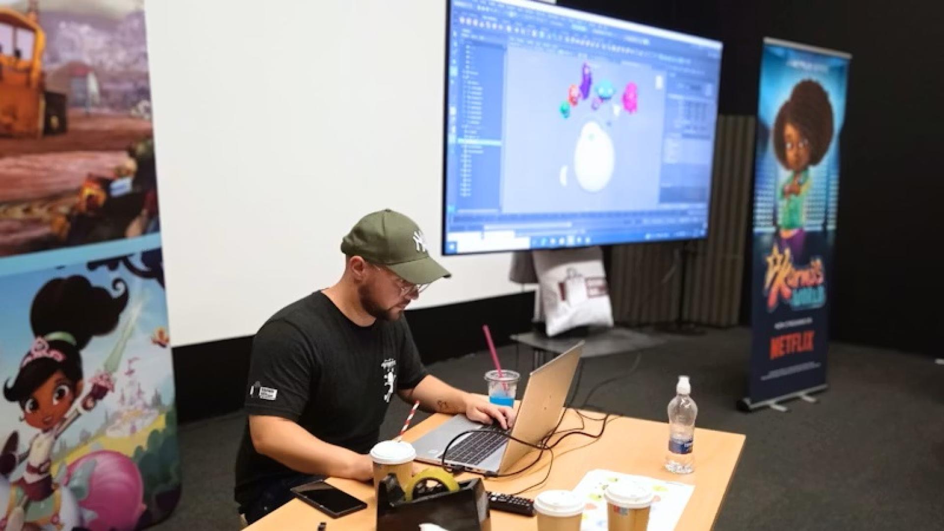 Person working on a laptop in front of a screen showing colorful 3D monster models during a workshop.