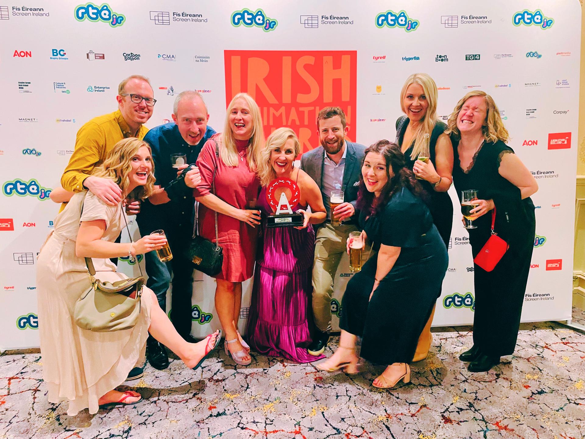 Large group posing in front of Irish Animation Awards backdrop with trophy held in center.