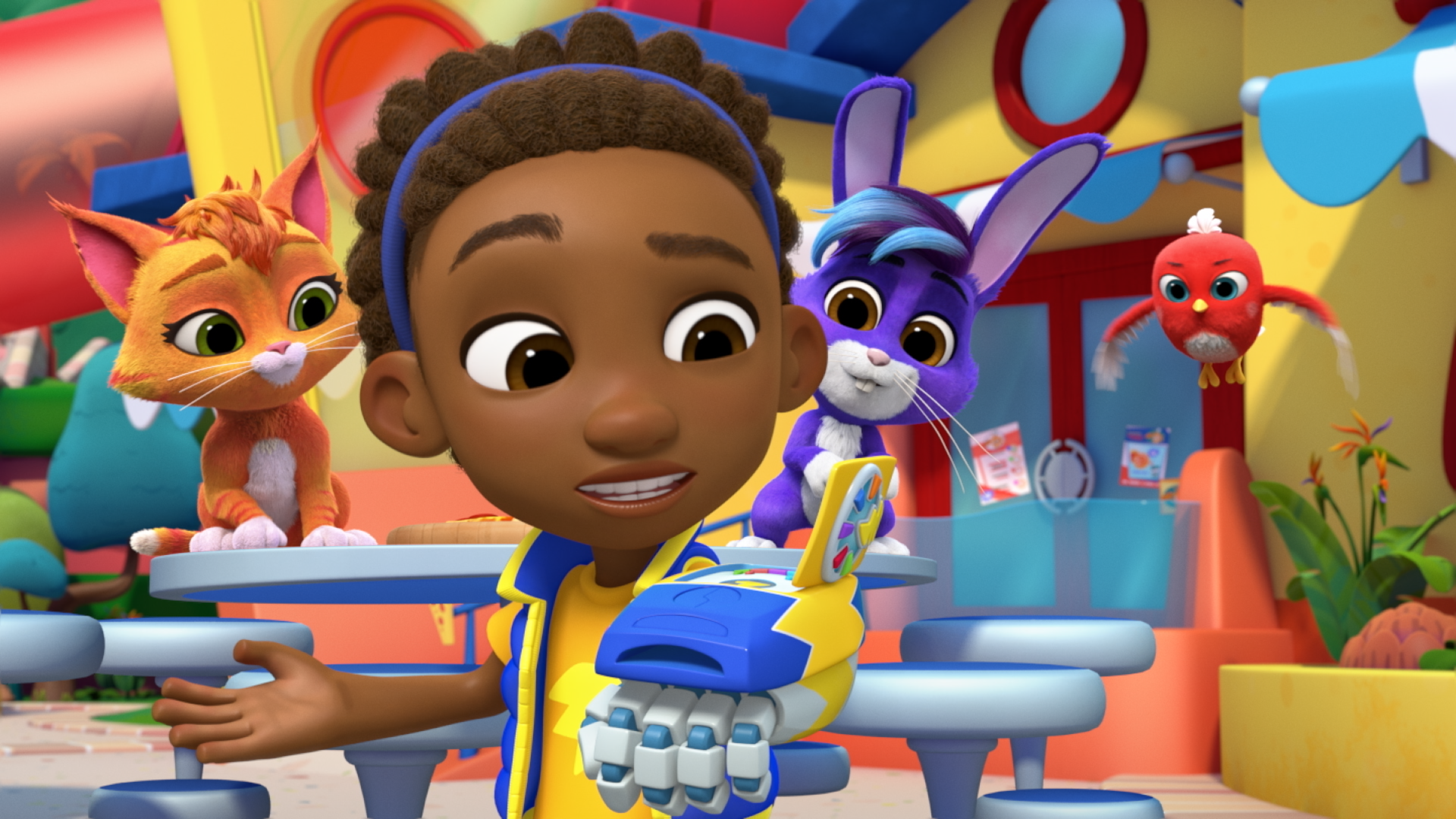 Animated production still from RoboGobo showing a bright, playful cafeteria setting where a child in a colorful outfit holds up a blue robotic glove device. Nearby, an orange cat and a purple rabbit look on with cheerful expressions, while a small red bird hovers in midair.