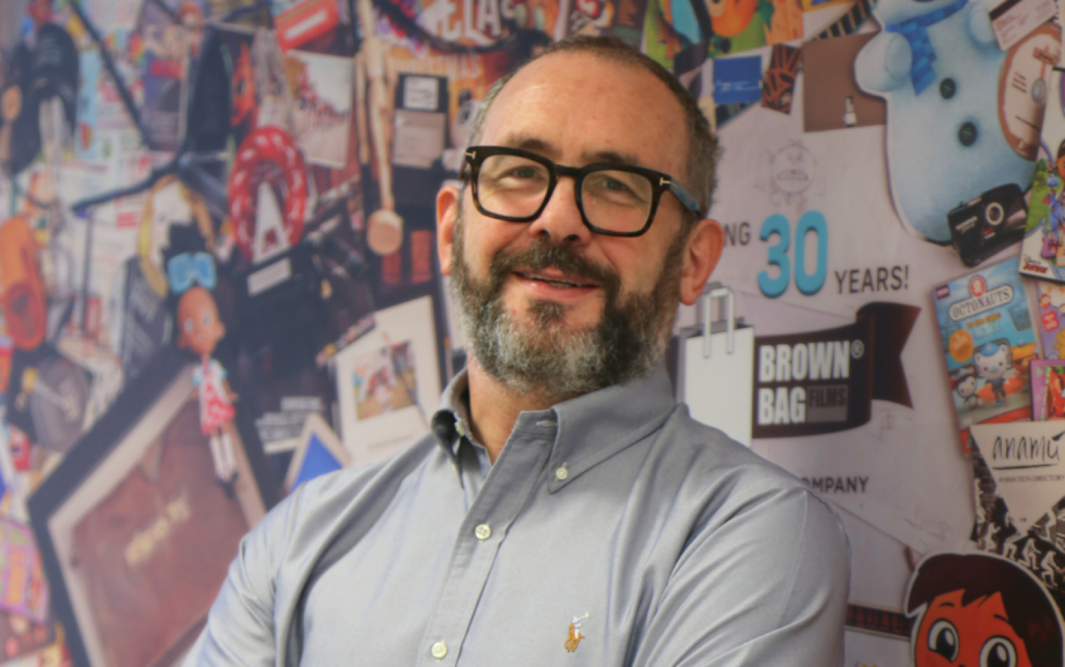 A photo of Cathal Gaffney, a colourful wall featuring a collage of Brown Bag Films' history behind him.