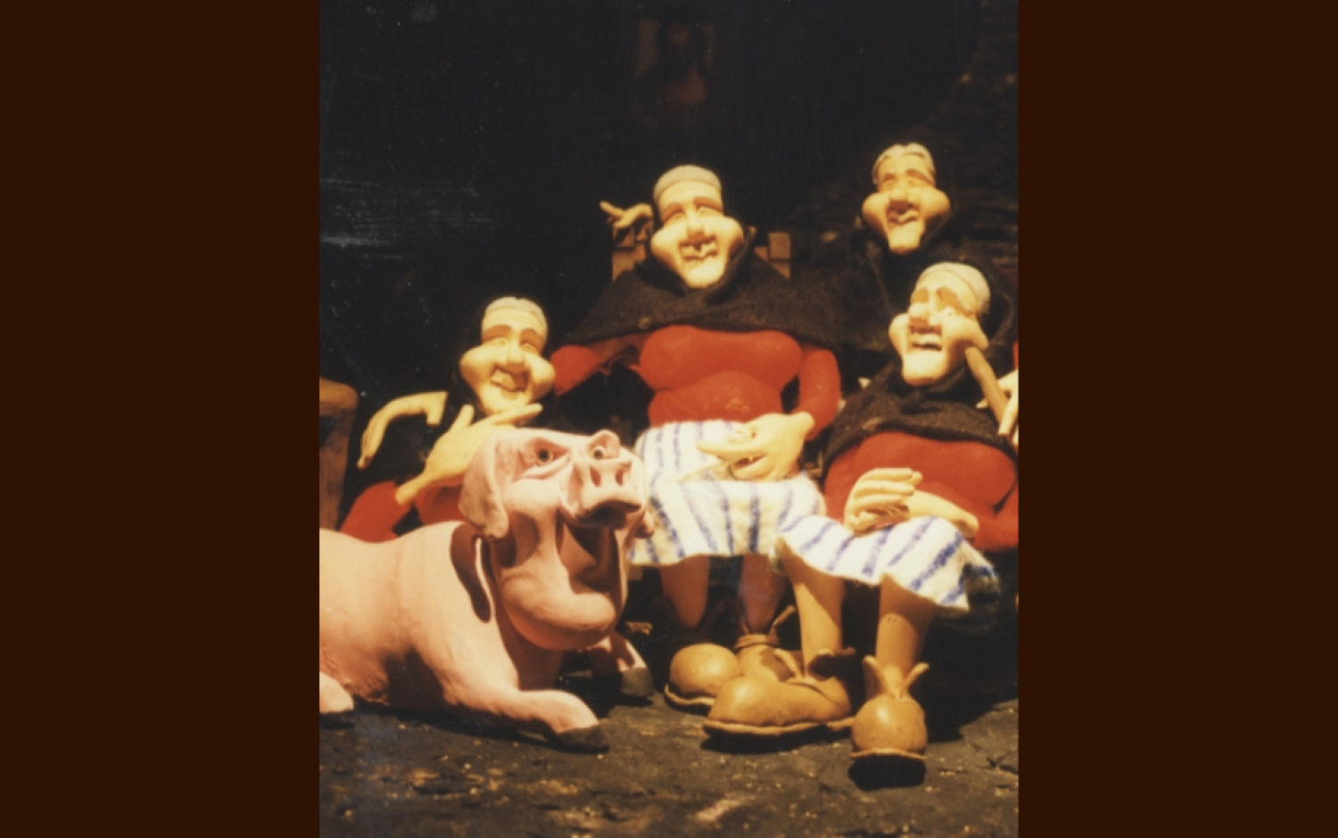 Stop-motion set featuring clay figures of four seated models of Peig Sayers and a pig in front of a dark backdrop.