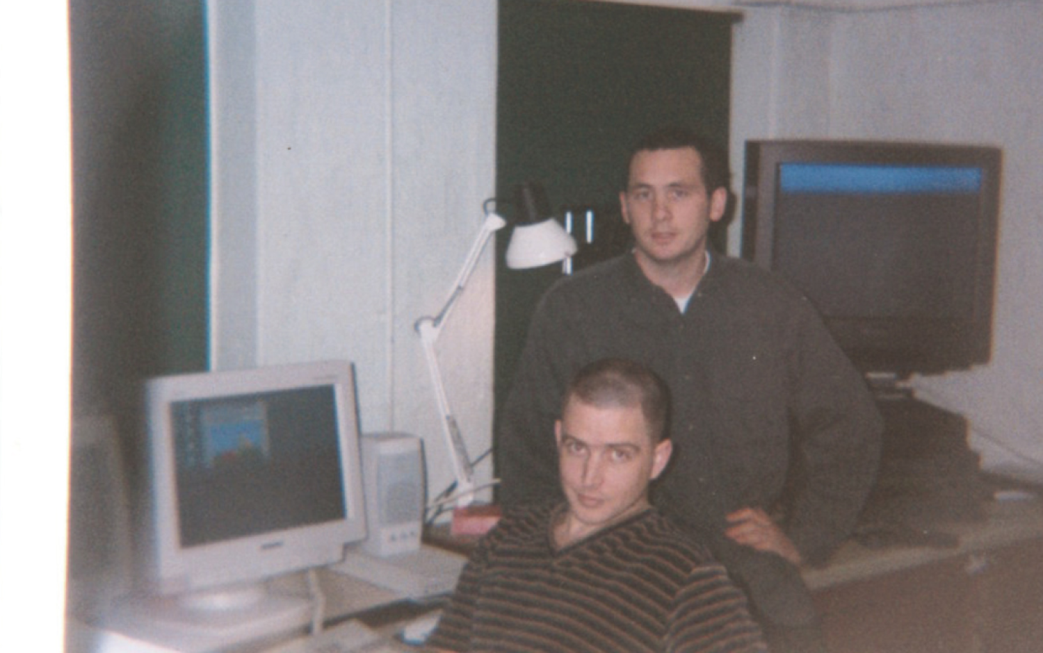 Two people in a studio with a computer and a TV screen displaying colorful animation.