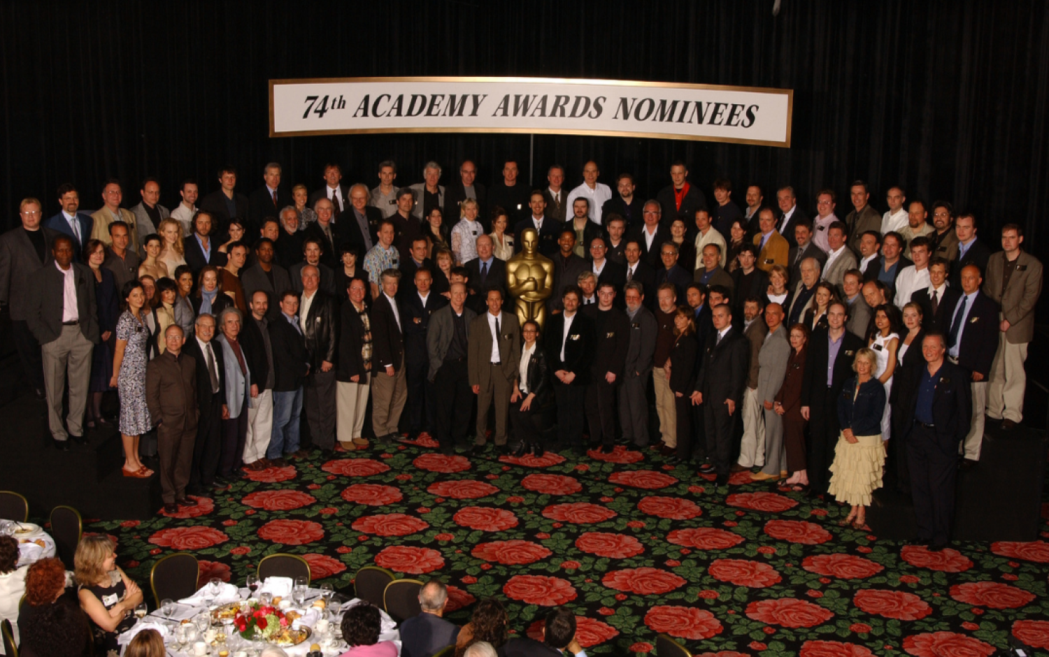 Large group photo of Academy Awards nominees posed on a stage with a golden Oscar statue and a banner reading “74th Academy Awards Nominees.”