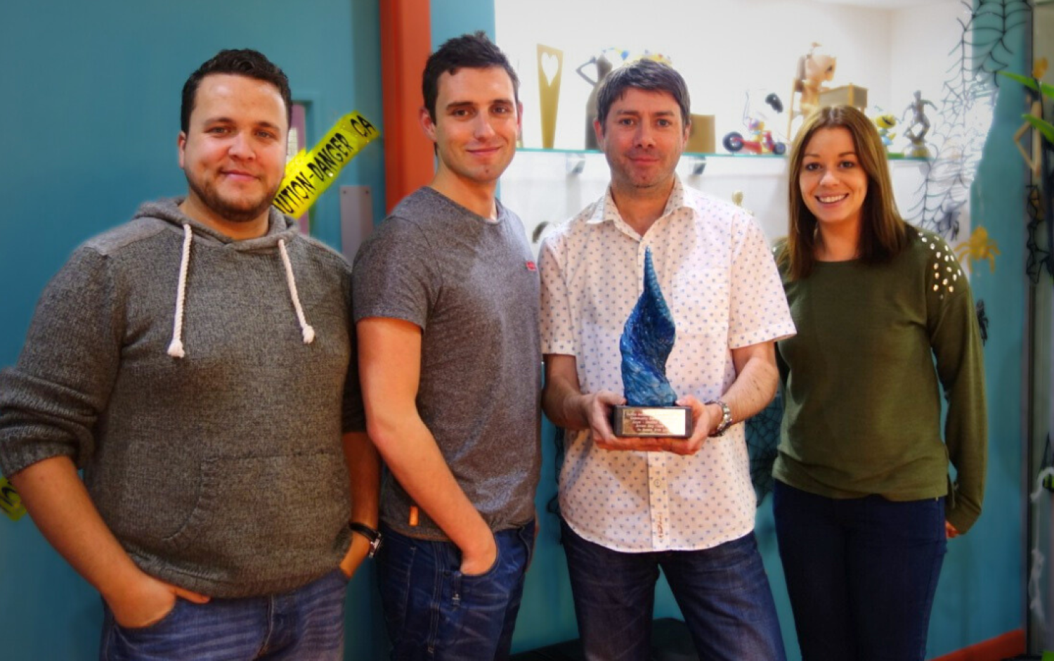 Four people standing indoors, one holding a blue sculpted award.