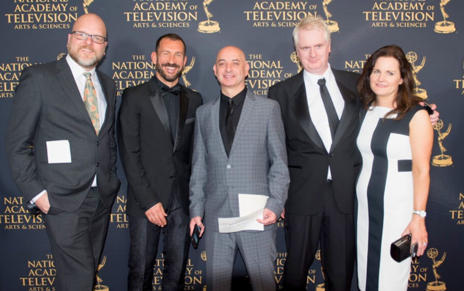 Group of five people posing on Emmy Awards red carpet in formal attire.