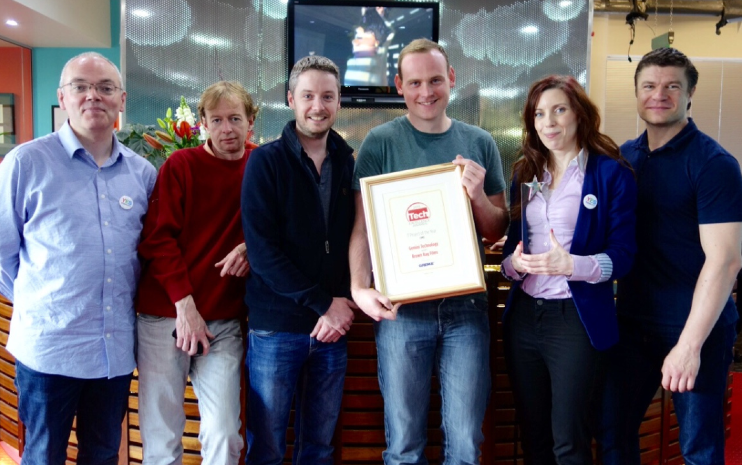 Six people standing indoors, holding a framed Tech Excellence Award certificate.