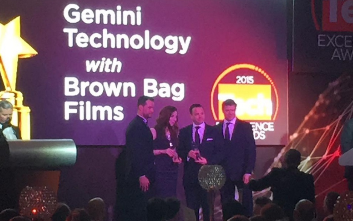 Group on stage at Tech Excellence Awards with screen displaying “Gemini Technology with Brown Bag Films.”