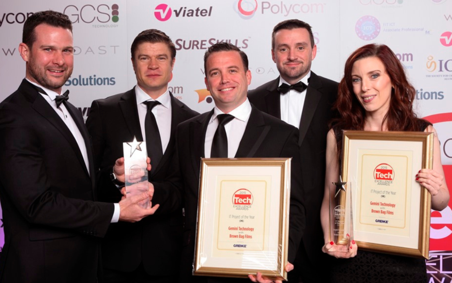 Group in formal attire posing with framed Tech Excellence Awards certificates and trophies.