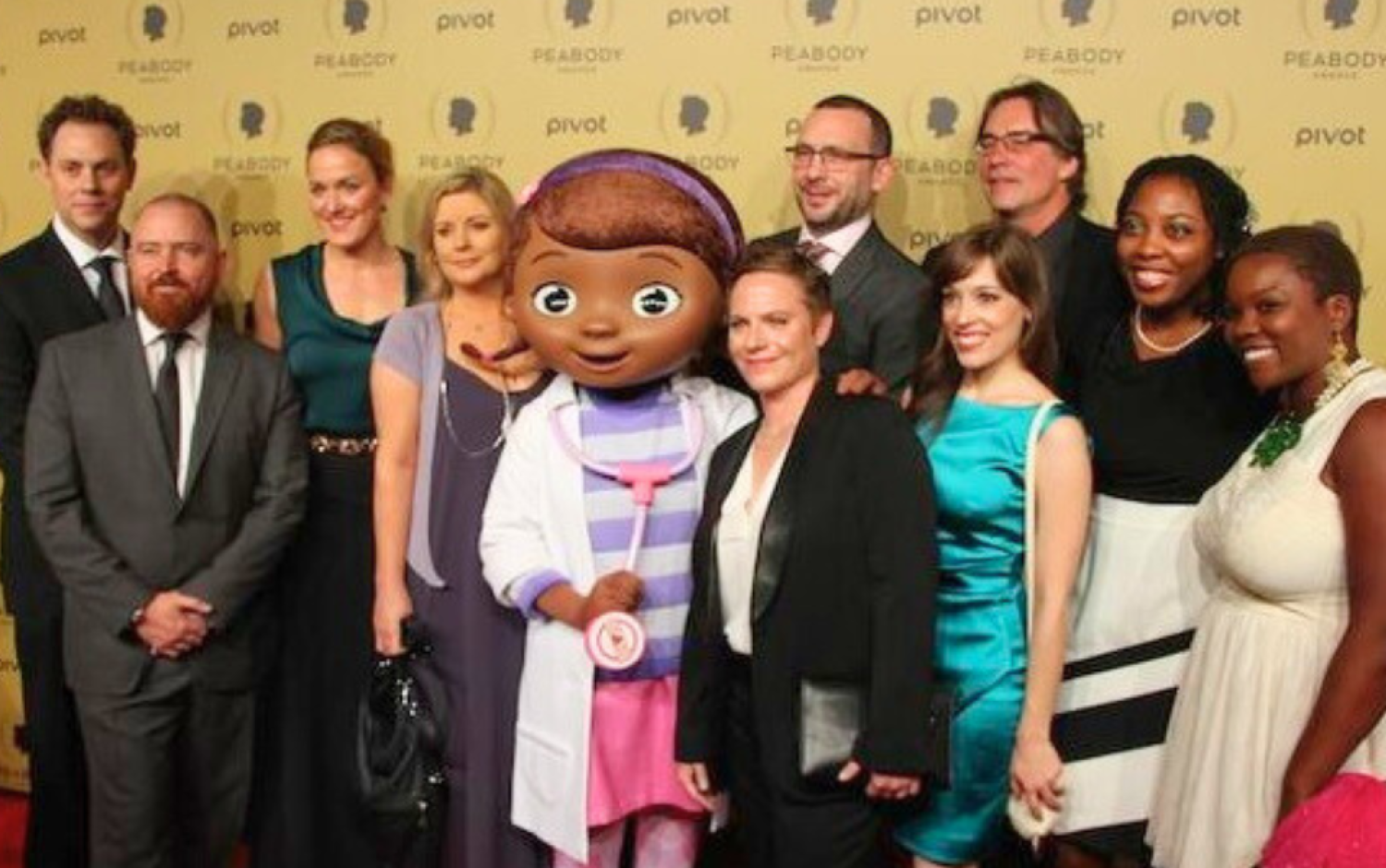 Group photo on Peabody Awards red carpet with mascot in center.