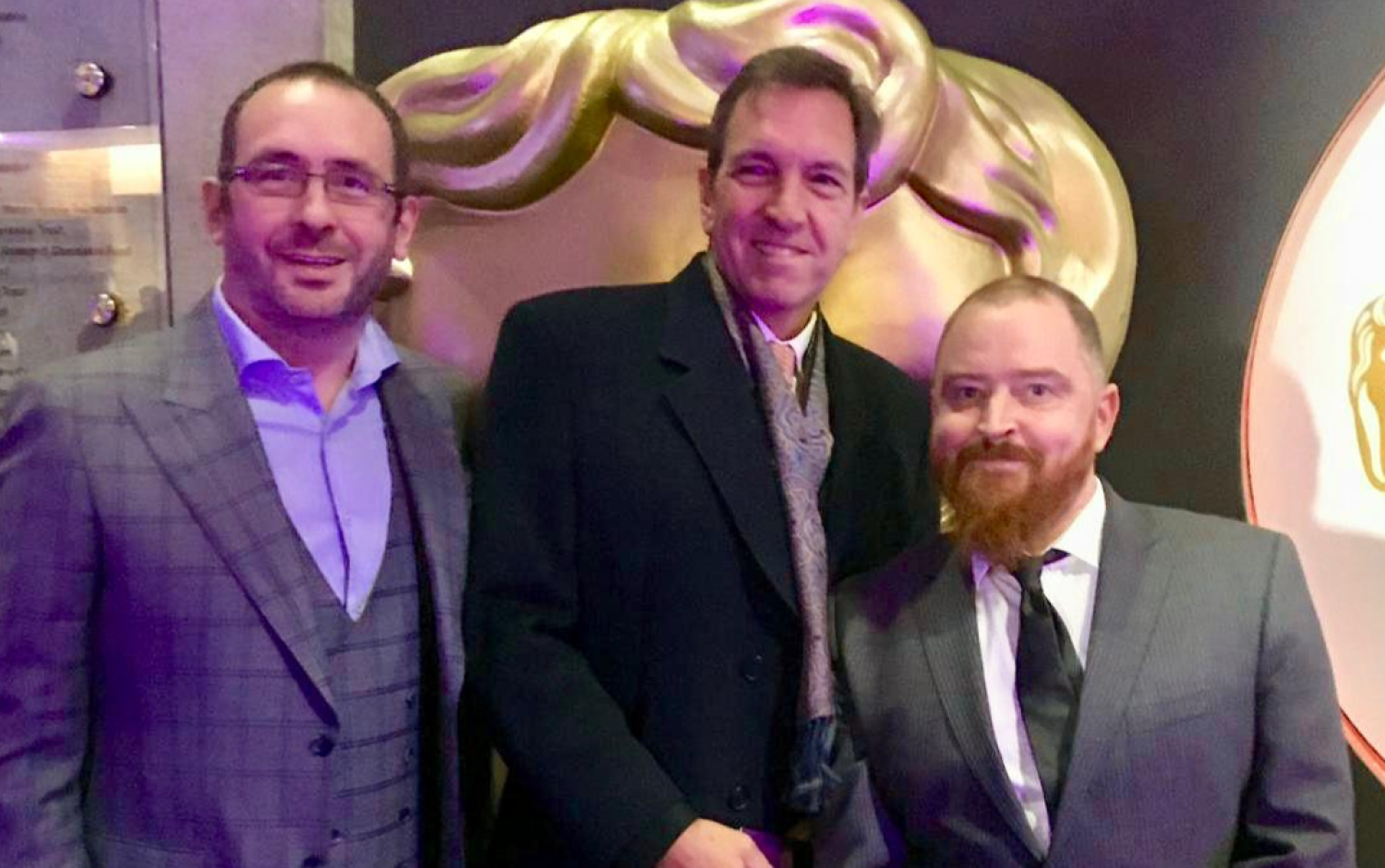 Group standing indoors near a large gold BAFTA mask display at an awards event.