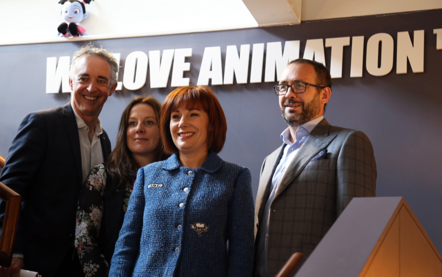 Group standing under a sign that reads “We Love Animation” inside an office space.