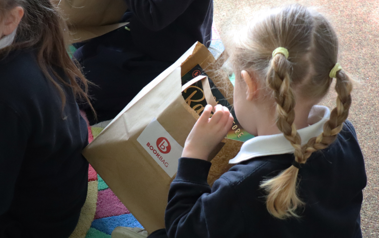 Close-up of a child holding a paper bag labeled “Bookbag” with books inside.