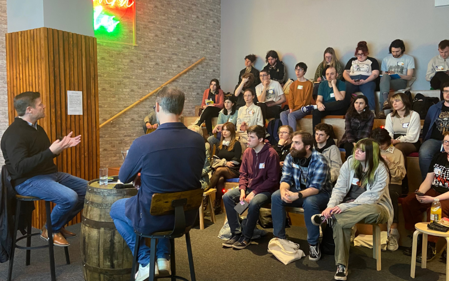 Audience seated in a casual venue listening to two speakers during a discussion session.