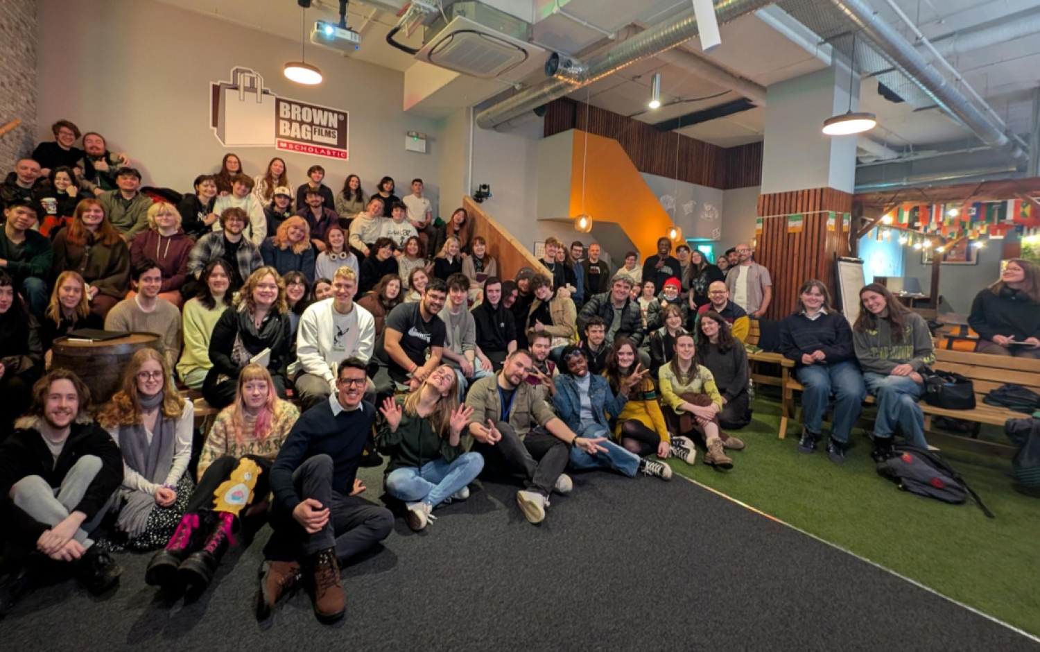 Wide group photo of people seated and standing in a modern office space during a company gathering.