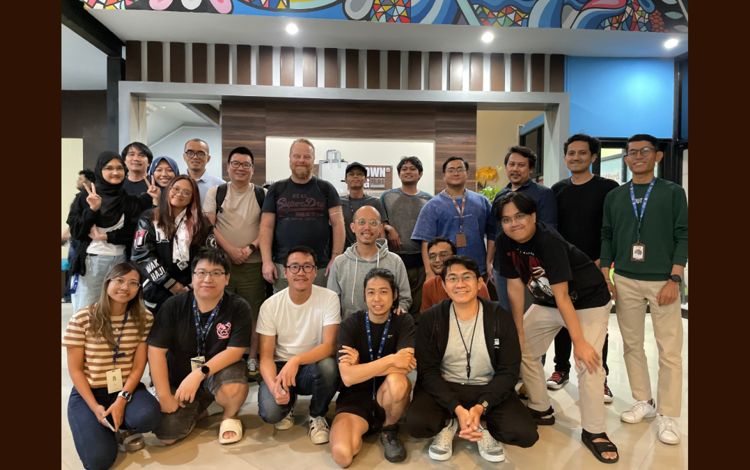 Group photo of people standing and kneeling in a brightly lit indoor space with colorful wall art above.